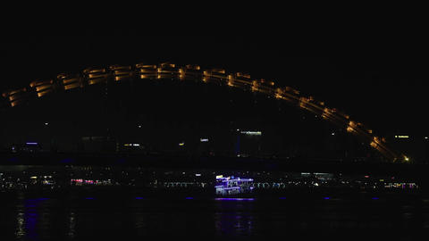 Close-up of Dragon bridge in Da Nang at night, ferry cruising under bridge