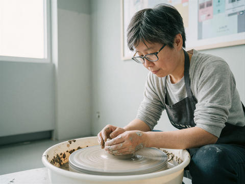 Asian woman crafting pottery on a wheel in a studio