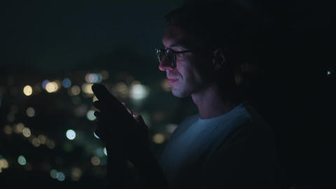 Side view portrait man wearing glasses using smartphone at night with city bokeh