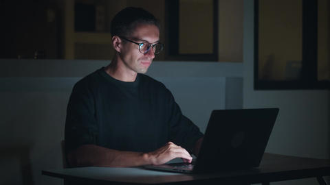 Man working on laptop at night from home, focused on screen and typing quietly