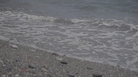 White-foamed waves lapping onto a dark, pebbly gray beach on an overcast day