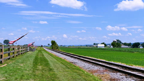 Train Tracks Stretch Through Green Fields Under a Blue Sky With Clouds in the