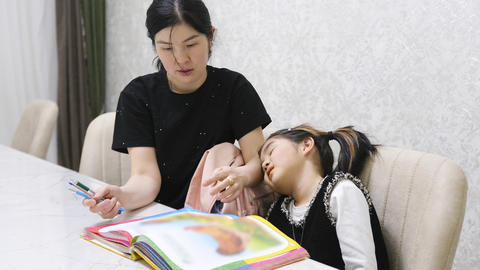 The little girl is tired and doesn't want to do her homework. Mom helps her little daughter with her