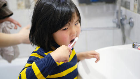 Close-up of a funny baby brushing her teeth with a toothbrush. A young Asian girl takes care of oral
