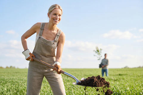 Active female gardener digging soil with a shovel in a green agricultural field
