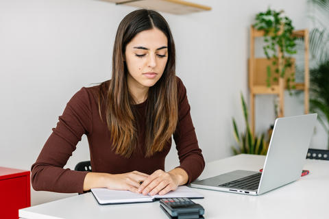 Young accountant using calculator while working on laptop computer at home