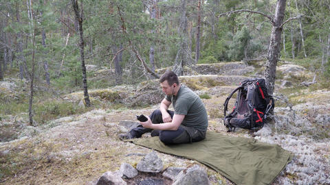 Hiker resting with smartphone at forest campsite