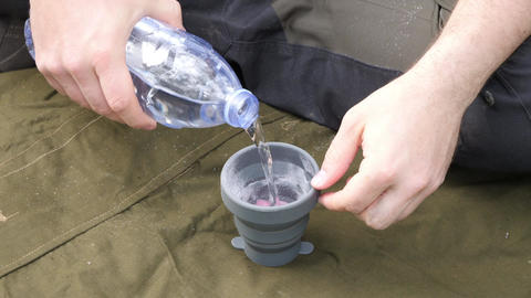 Hands pouring water into collapsible camping cup outdoors