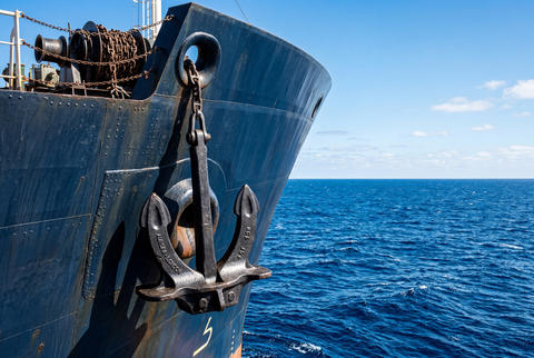 Heavy black metal anchor attached to the bow of a large ship sailing on the blue ocean
