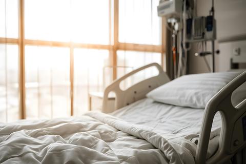 Empty hospital room with a neatly made patient bed bathed in soft warm sunlight from the large windo