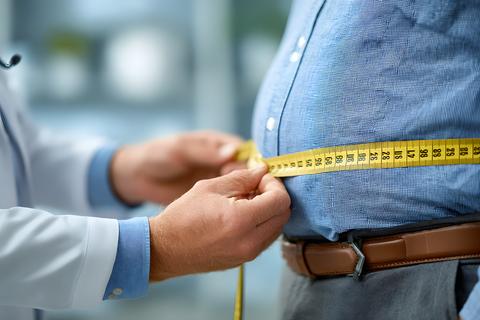 Medical professional using a measuring tape to assess the waist circumference of an overweight patie