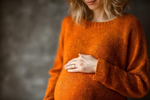 Peaceful pregnant woman gently holding her beautiful rounded belly with one hand wearing a comfortab