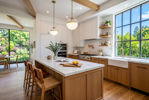 Modern kitchen interior with central island white cabinets and large windows overlooking green yard