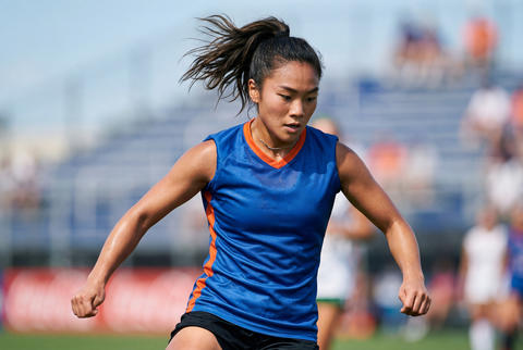 Athletic asian female soccer player running during a competitive match on field