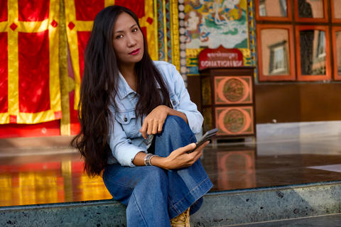 Asian girl sitting on temple floor with smartphone in hand