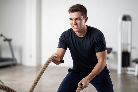 Determined young man exercising with battle ropes in a modern gym
