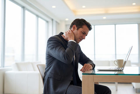 Businessman suffering from neck pain due to stress and bad posture at his modern office workplace
