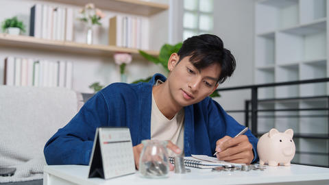 Asian man in 20s planning home savings budget with coins and piggy bank