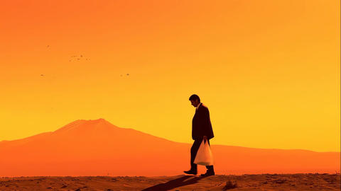 Silhouette of a man walking toward a distant mountain during a bright orange sunset
