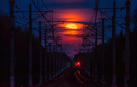 Red full moon rising over railroad tracks at twilight
