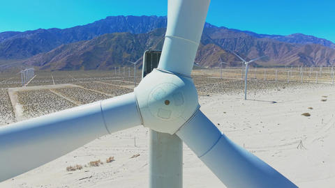 Extreme close aerial view of wind turbine mechanism in Palm Springs desert with mountains in