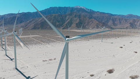 Close aerial drone shot of giant wind turbines in Palm Springs desert with mountains and clear