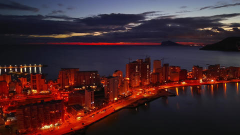 Sunset Over Tranquil Seaside City. Evening Seascape Featuring Glowing Streets And Distant Islands