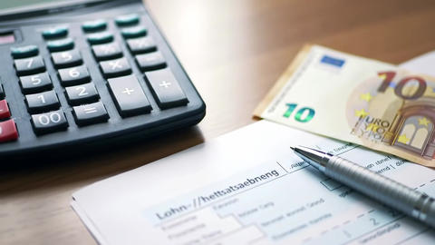 A calculator euro bill and pen rest on a wooden desk surface