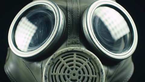 A close up shows an olive green gas mask with circular lenses