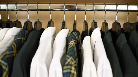A closet shows white shirts dark green shirts and a plaid shirt hanging