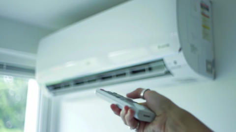 Hand holds a remote pointing at a white wall mounted air conditioner