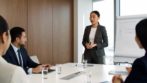 Smiling Asian woman presents at a meeting in a gray pinstripe suit