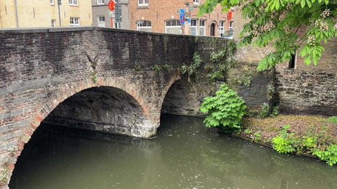 Rainy day on old town canal with stone bridge, spring rain falling on water surface