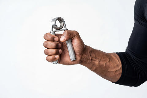Muscular forearm and hand squeezing a metal grip strengthener on a white background