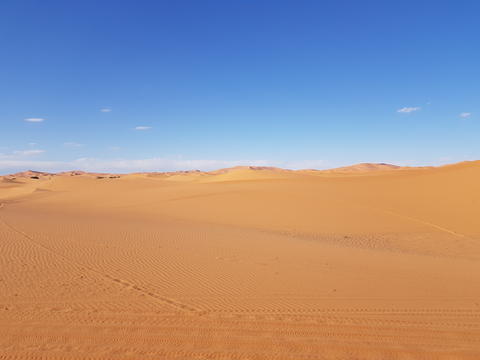 A desert landscape with a blue sky and footprints in the sand
