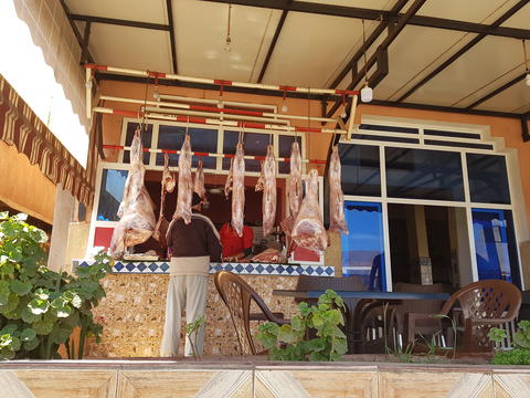 A man stands in front of a butcher shop with meat hanging