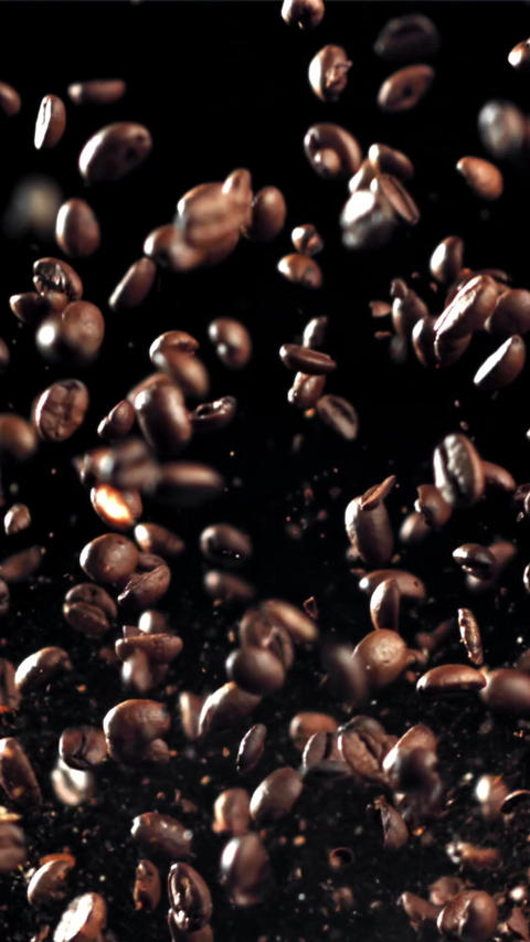Coffee beans fly in different directions. On a black background. Filmed on a