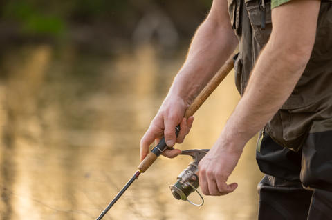 Close up of fisherman hands reeling fishing line with spinning rod. Outdoor