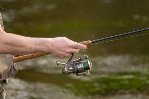 Close-up of fisherman hands handling spinning reel and fishing rod while fly