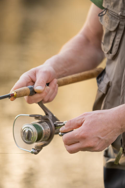 Close-up of fisherman hands handling spinning reel and fishing rod while fly