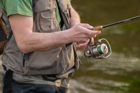 Close-up of fisherman hands handling spinning reel and fishing rod while fly