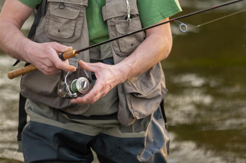 Close-up of fisherman hands handling spinning reel and fishing rod while fly