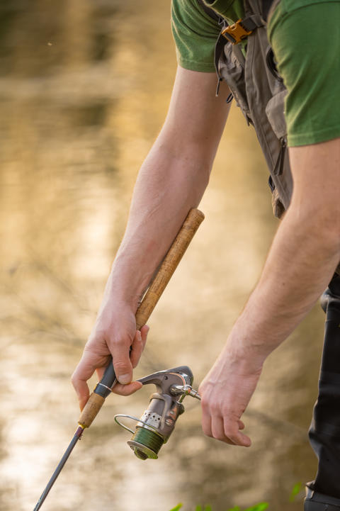 Close-up of fisherman hands handling spinning reel and fishing rod while fly