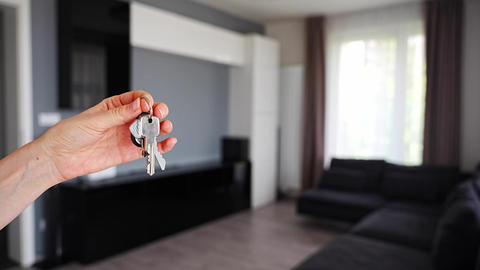 Hand holding apartment keys in furnished resale apartment living room interior