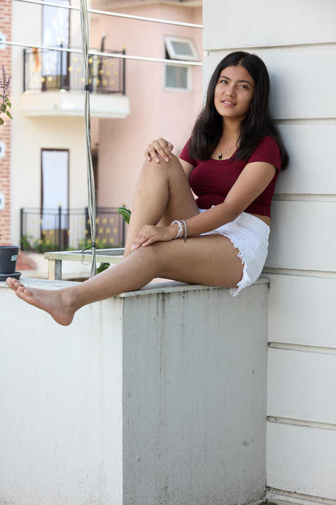 Asian girl in maroon crop top and white skirt seated on windowsill barefoot