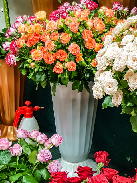 Colorful bouquet of roses in various shades arranged in a tall white vase with a spray bottle