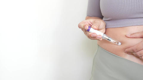 Woman injecting GLP-1 weight loss medication into stomach on light background
