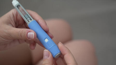 Woman setting dosage clicks on GLP-1 injection pen close-up