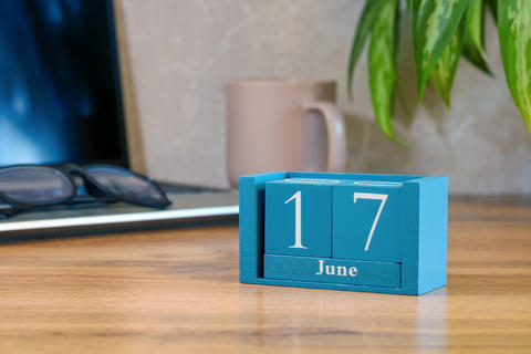Blue desk calendar showing 17 June on office desk with laptop glasses and coffee mug for planning