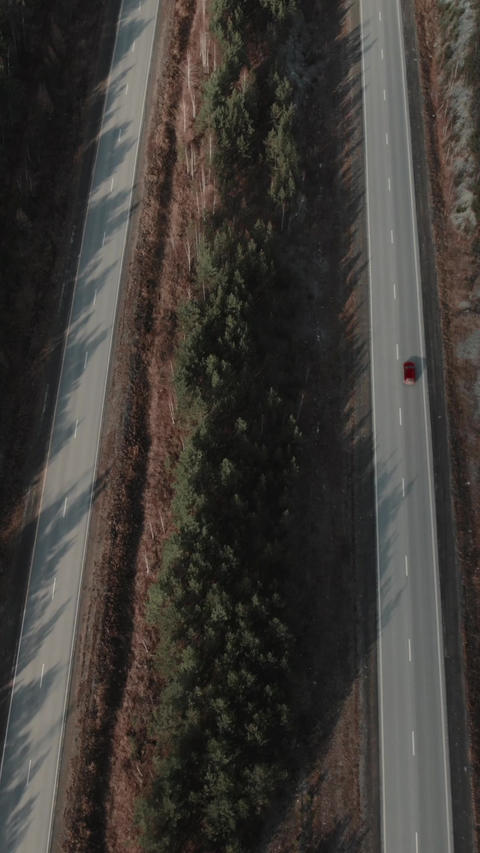 Aerial top down footage of red car driving on highway beside forest trees